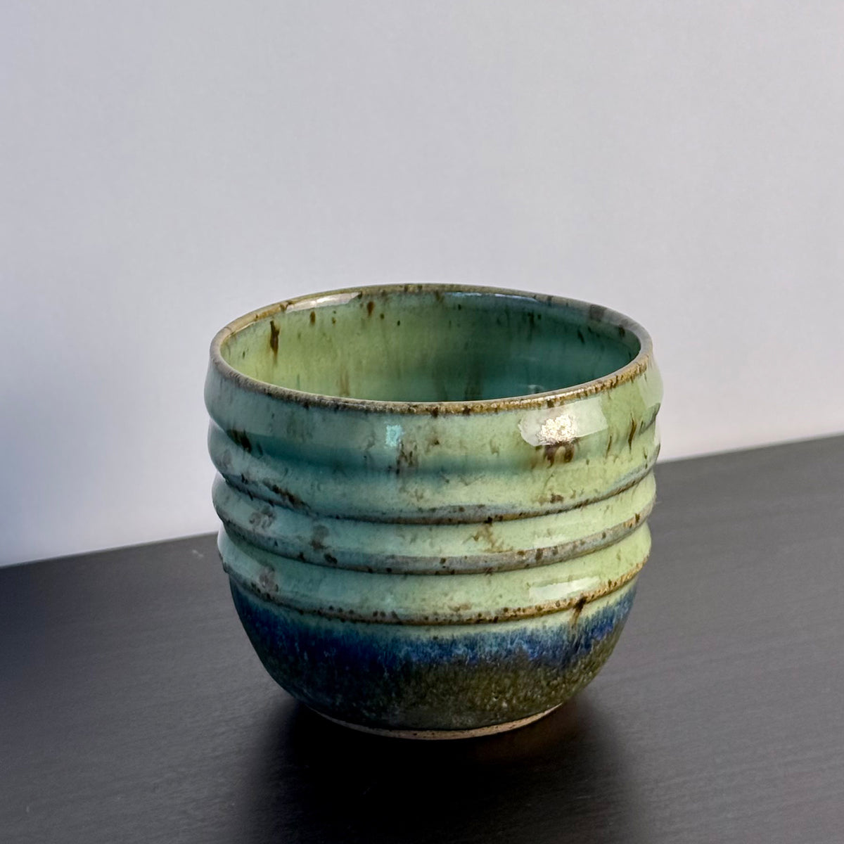 Small handmade Olive Groove Pot with a rounded shape, carved horizontal bands, and glossy olive-green glaze that shifts to deep blue-green and earthy brown near the base.