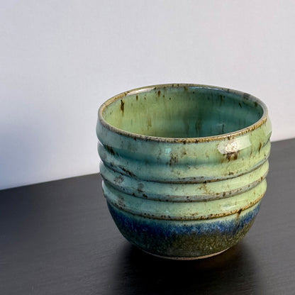 Small handmade Olive Groove Pot with a rounded shape, carved horizontal bands, and glossy olive-green glaze that shifts to deep blue-green and earthy brown near the base.