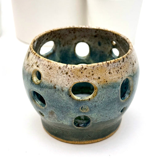 Handmade ceramic luminary with a deep teal glaze and oval cutout openings.