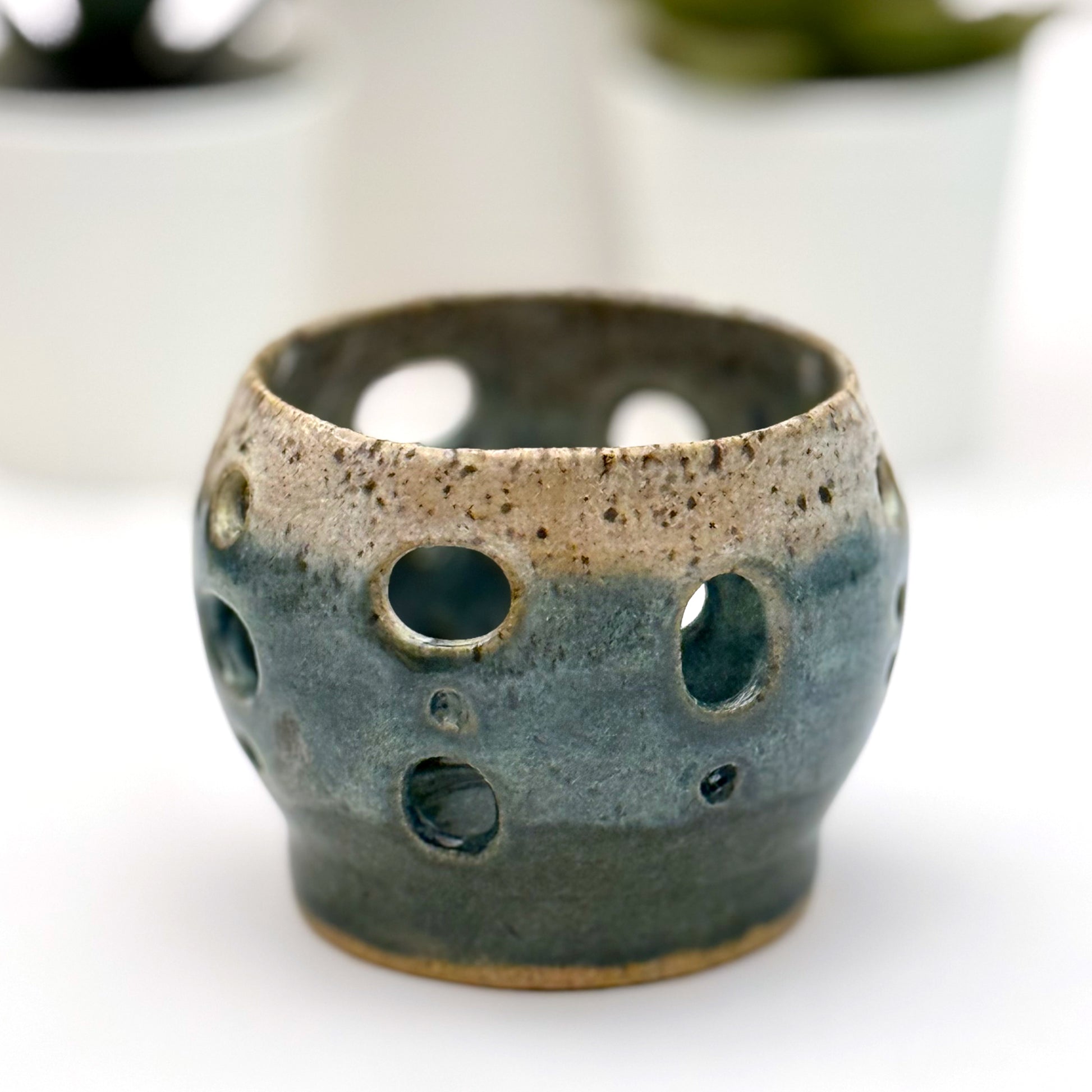 Handmade ceramic luminary with a deep teal glaze and oval cutout openings.