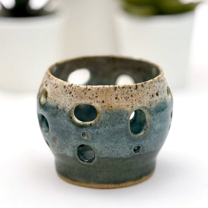 Handmade ceramic luminary with a deep teal glaze and oval cutout openings.