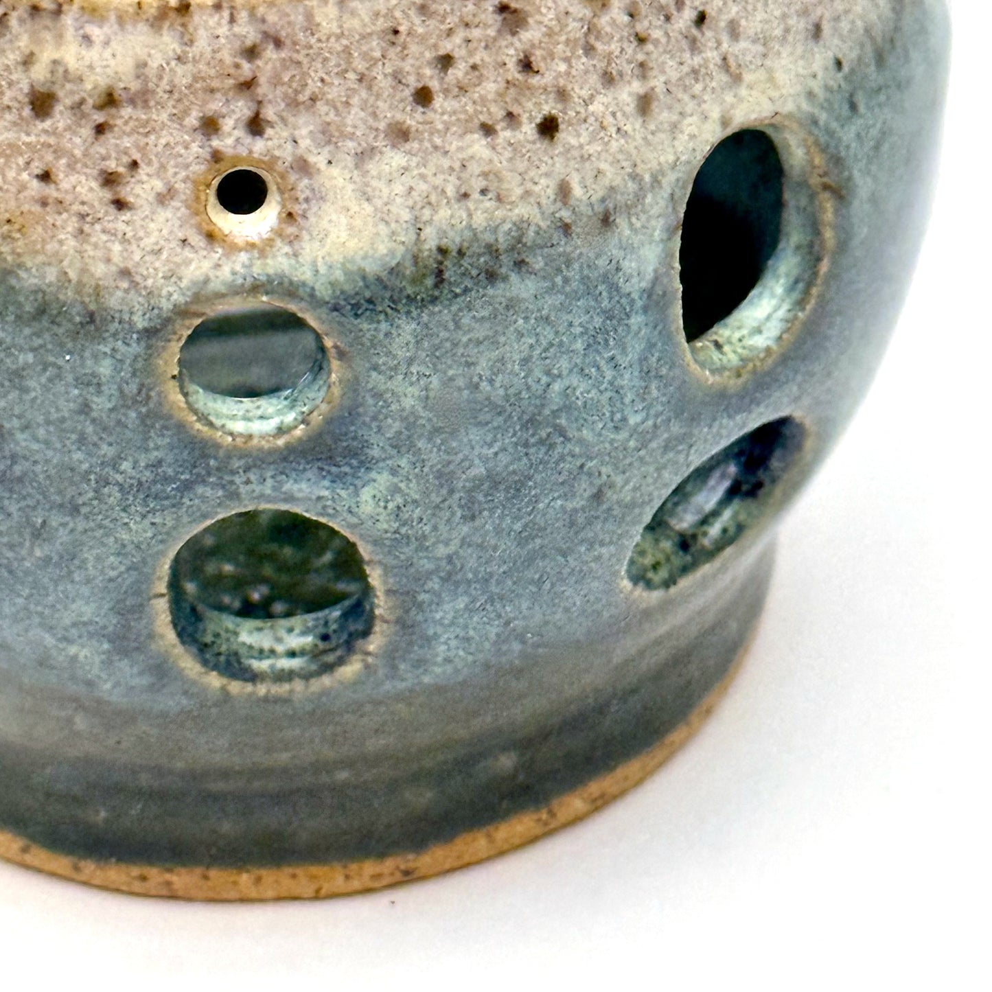 Close-up of a handmade ceramic luminary with a deep teal glaze and oval cutout openings.