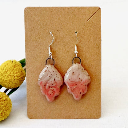 Pink speckled earrings on a brown card with yellow flowers in the background