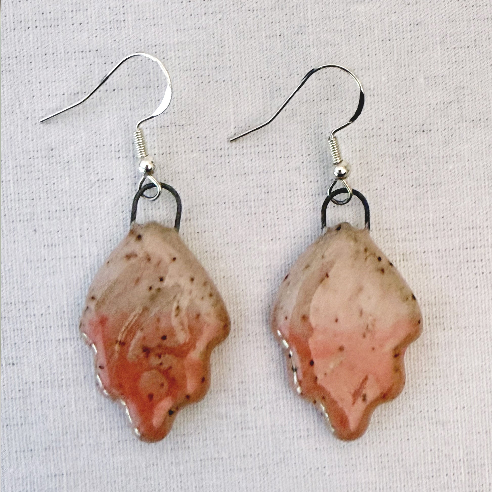 Pair of earrings with pink and brown speckled design on a light fabric background