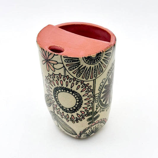 Handmade 14oz stoneware mug with mid-century inspired floral pattern and warm coral pink glazed top. The graphic flower design wraps around the exterior, and the mug features a cutout sip opening.