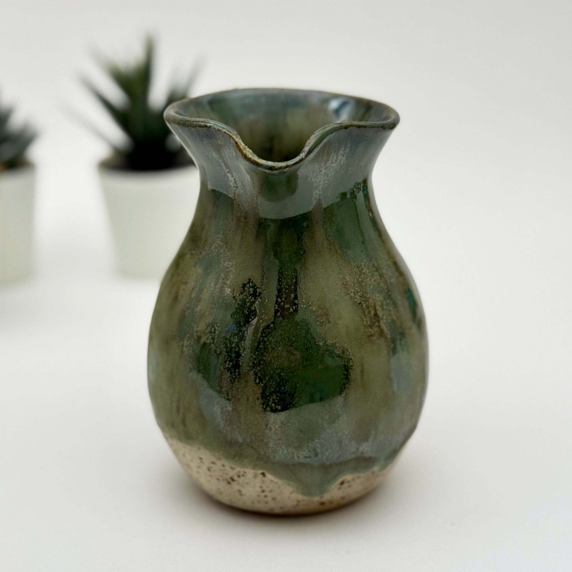 Green ceramic vase on a white surface with blurred plants in the background