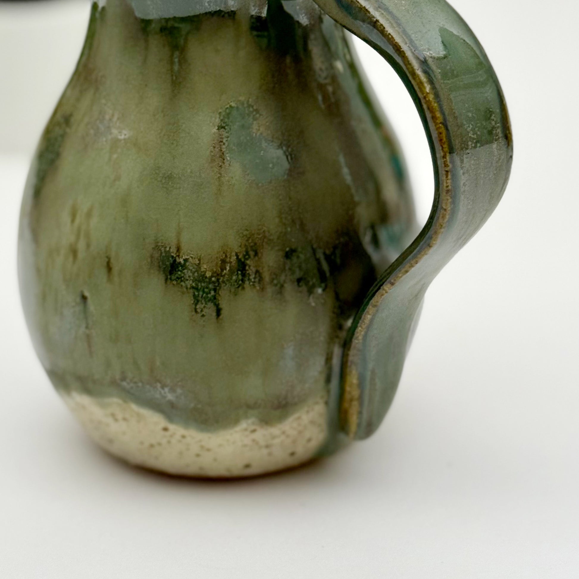 Cloese-up of Green ceramic pitcher with a handle on a white background