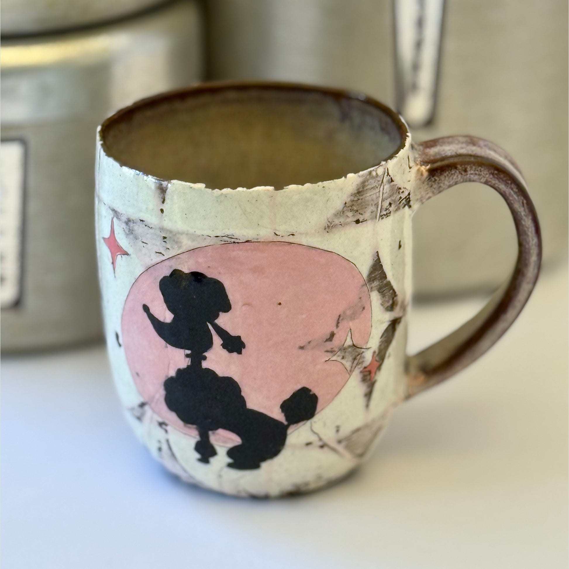 Pink-and-white ceramic mug featuring a black retro poodle silhouette against a pink circle.
