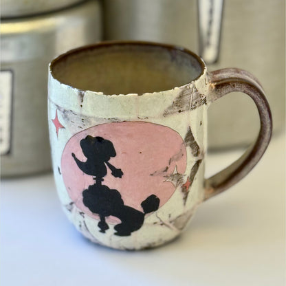 Pink-and-white ceramic mug featuring a black retro poodle silhouette against a pink circle.
