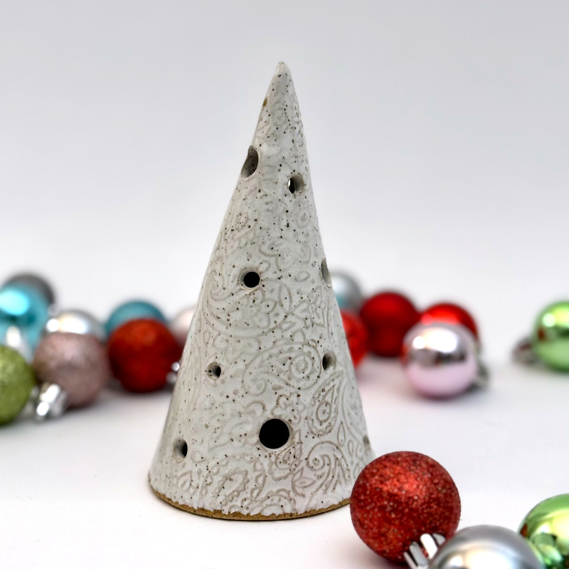 A handcrafted white paisley-textured ceramic tree with light holes, displayed with assorted holiday ornaments.
