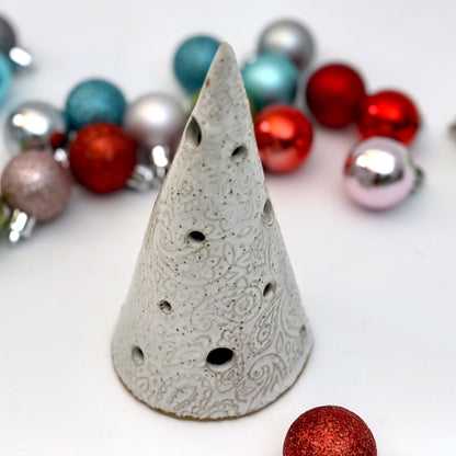 A handcrafted white paisley-textured ceramic tree with light holes, displayed with assorted holiday ornaments.