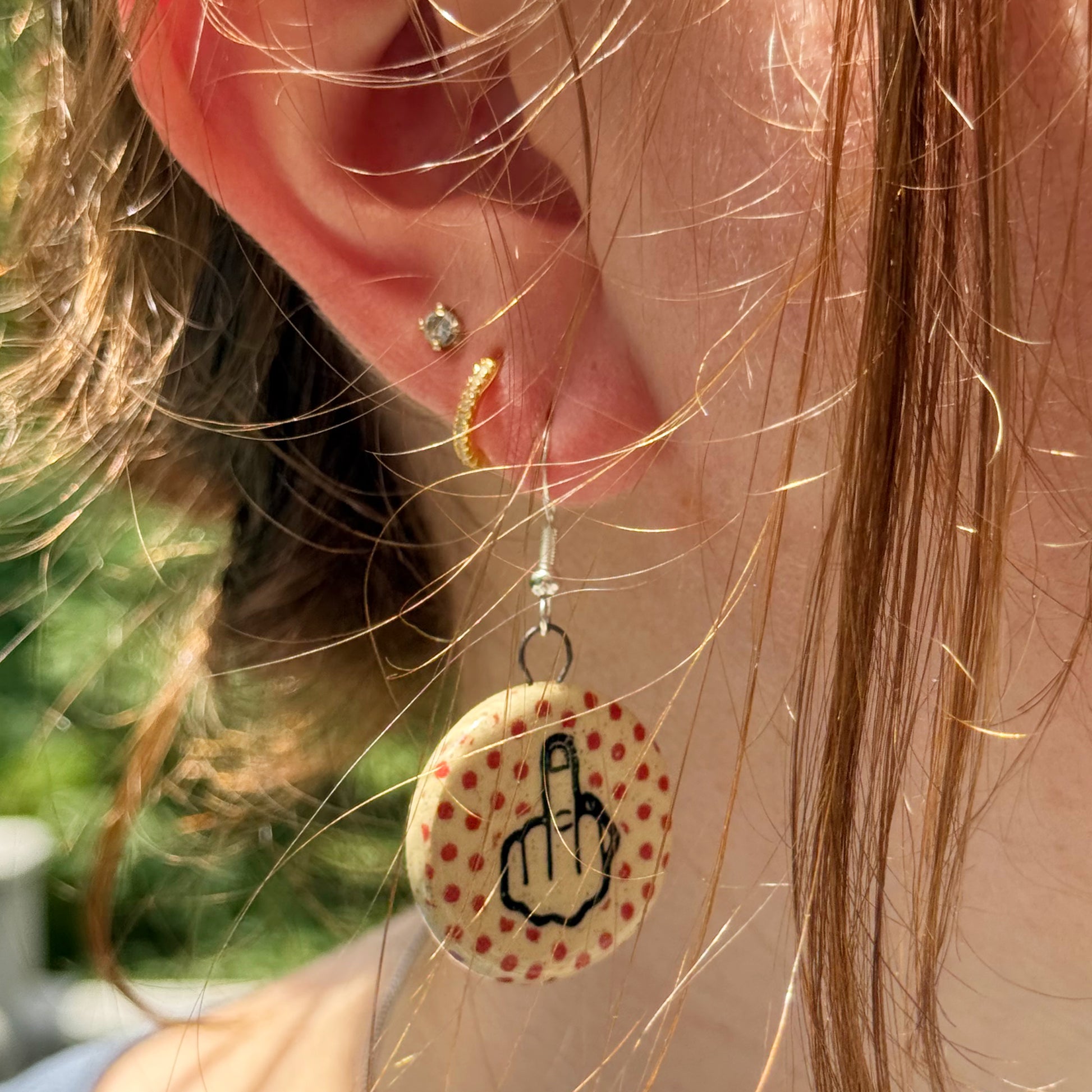 Close-up of an earring with middle finger and polka dot design, worn by a person.