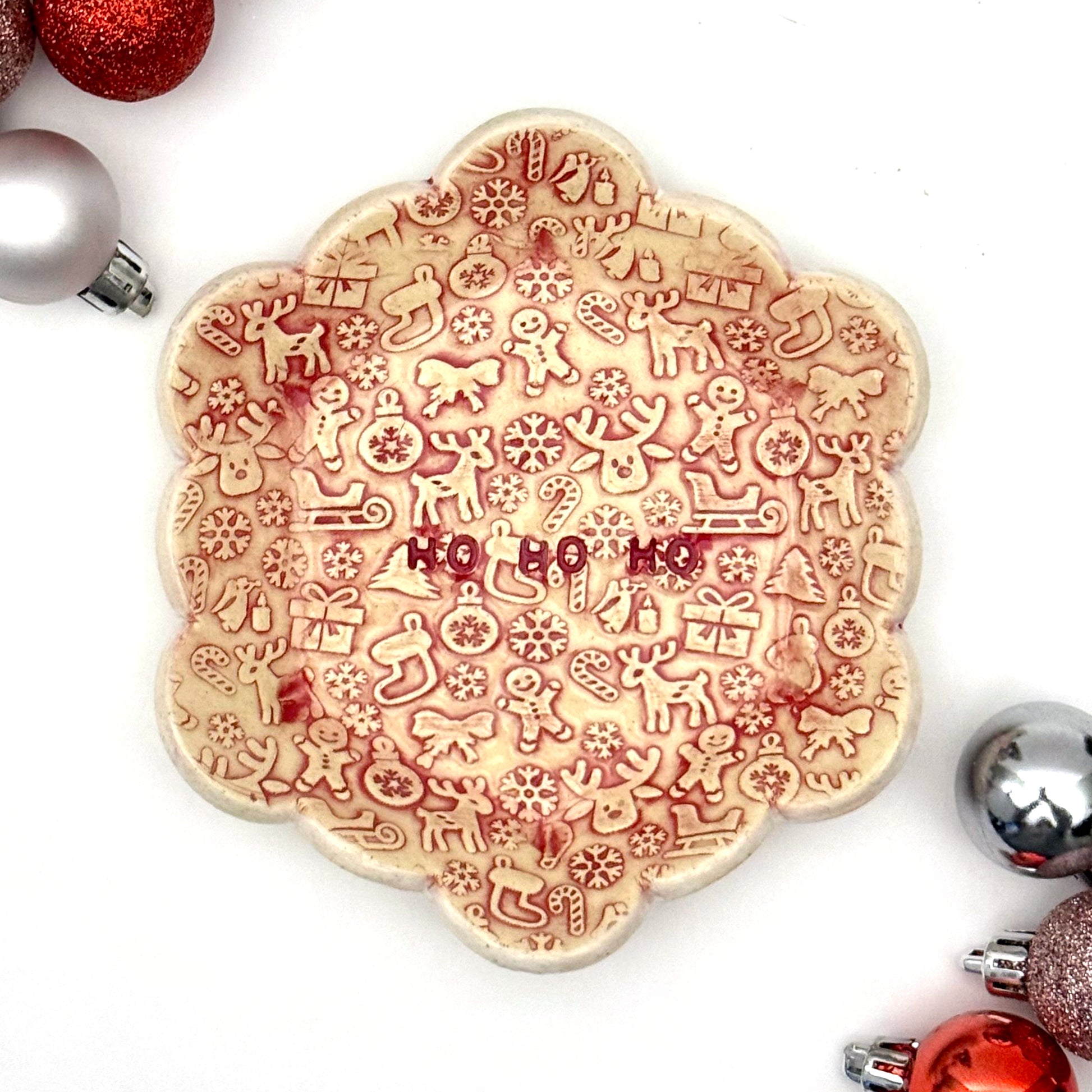 Decorative cookie with Christmas-themed designs and 'HO HO HO' text, surrounded by festive ornaments on a white background.