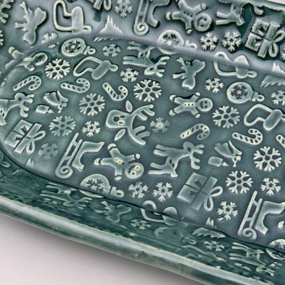 Close-up of a decorative green plate with holiday patterns on a white background with colorful ornaments.