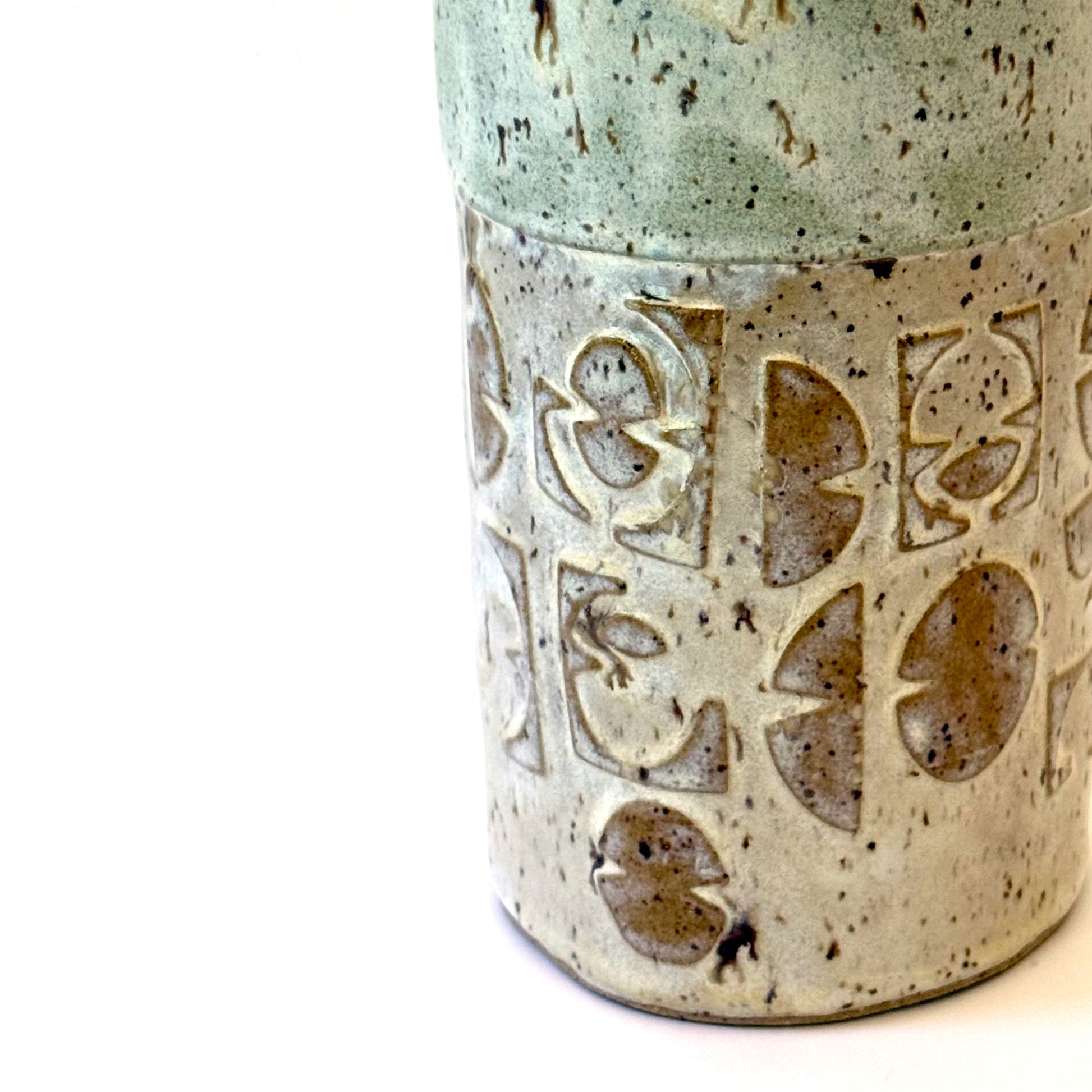 Close up of handmade stoneware vase with layered green glaze over textured surface and speckled clay base.