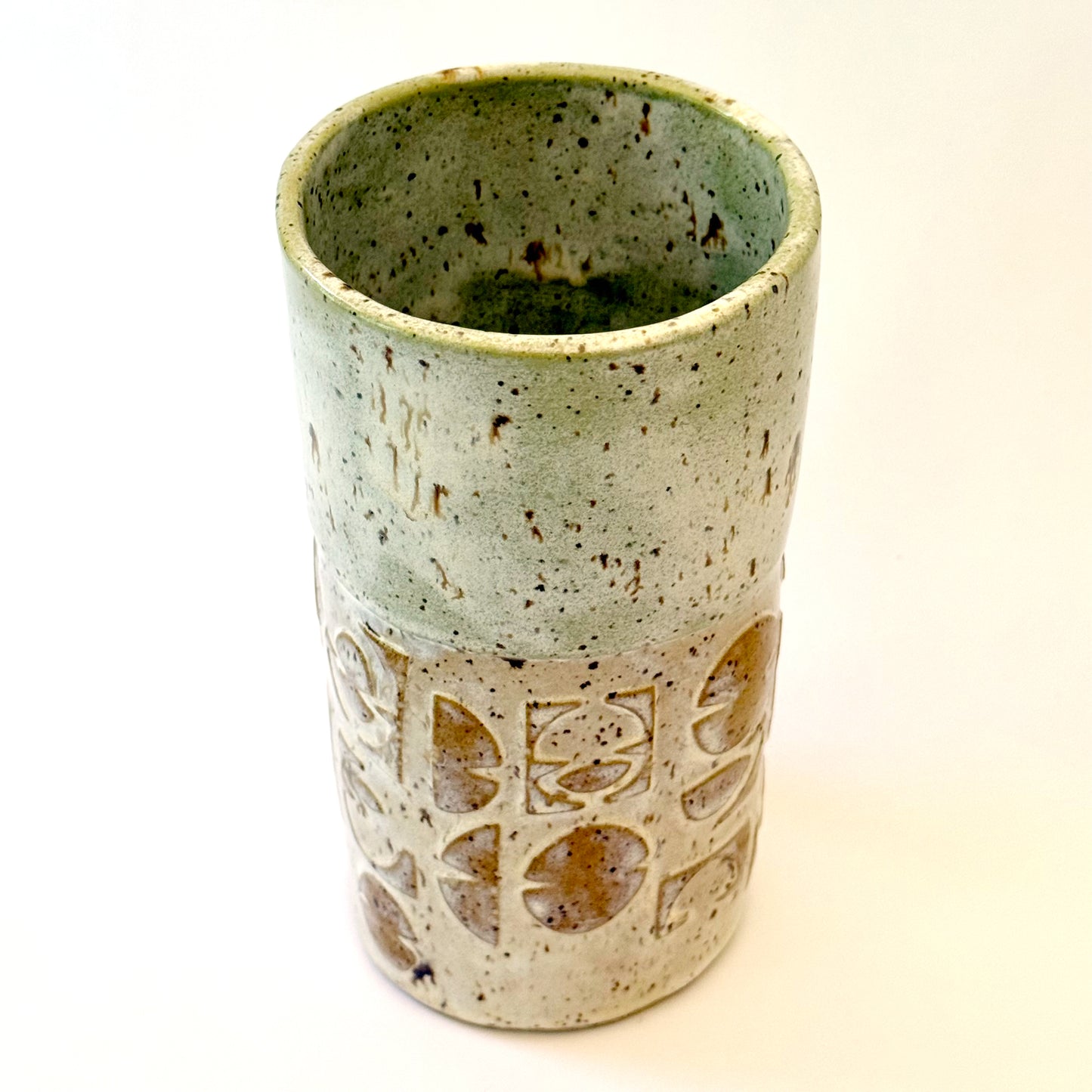 Handmade stoneware vase with layered green glaze over textured surface and speckled clay base.