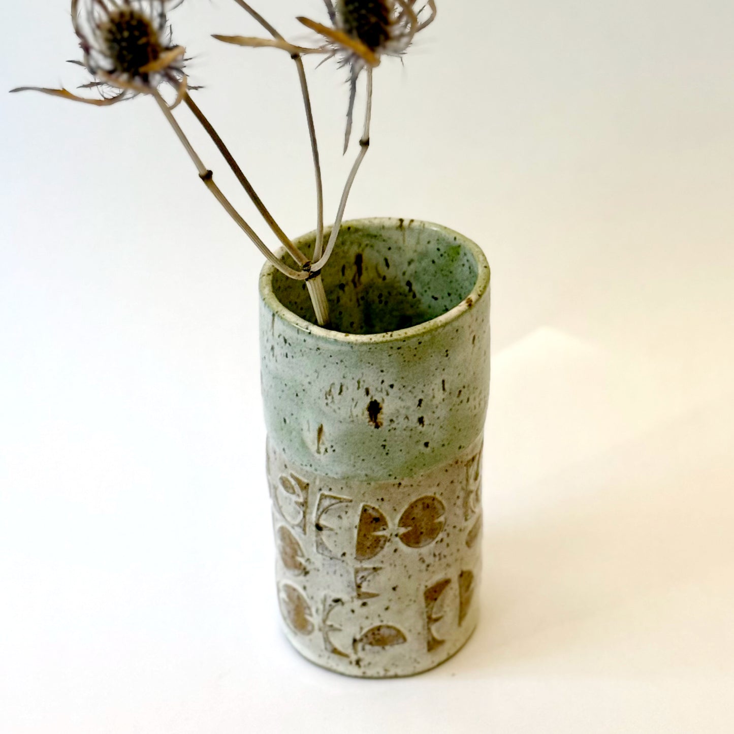 Handmade stoneware vase with layered green glaze over textured surface and speckled clay base.