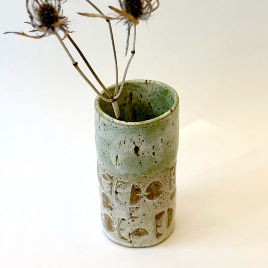 Handmade stoneware vase with layered green glaze over textured surface and speckled clay base.