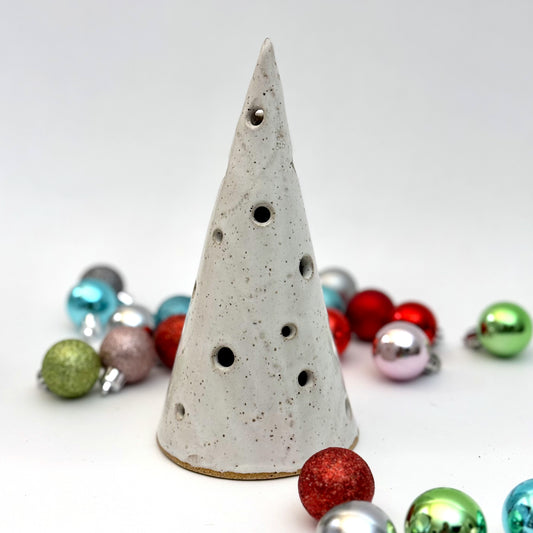 A white speckled ceramic tree luminary with round cutout holes, surrounded by colorful holiday ornaments.