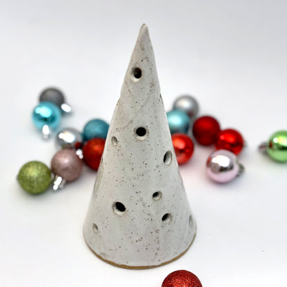 A white speckled ceramic tree luminary with round cutout holes, surrounded by colorful holiday ornaments.