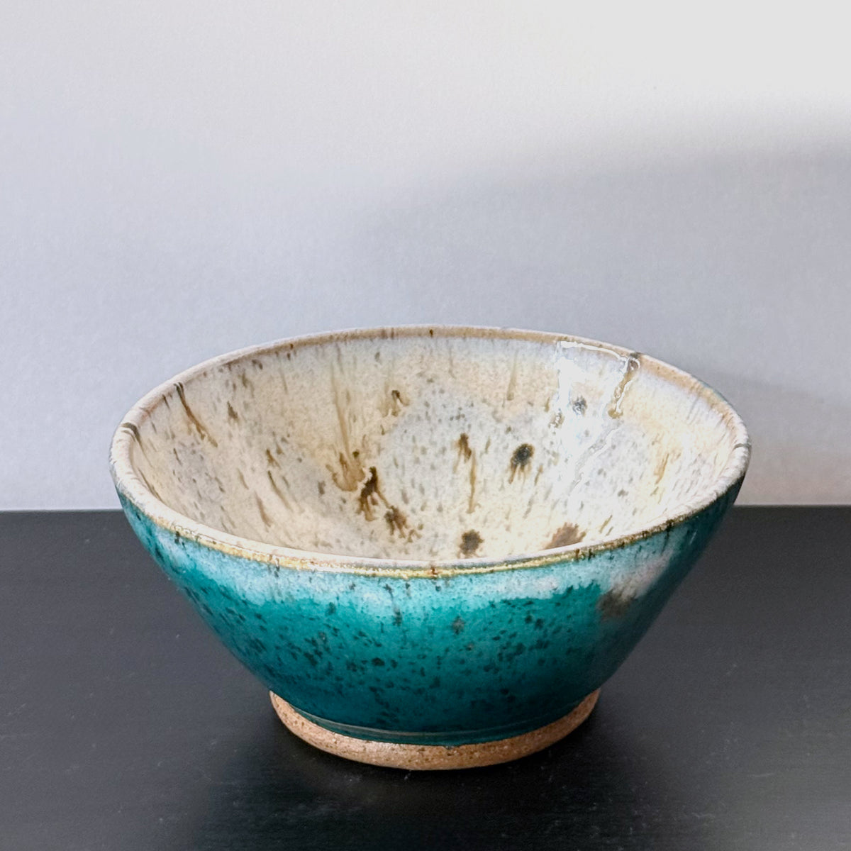 Handmade ceramic bowl with a saturated teal exterior and a creamy speckled interior, finished with a wide rounded profile and glossy glaze.