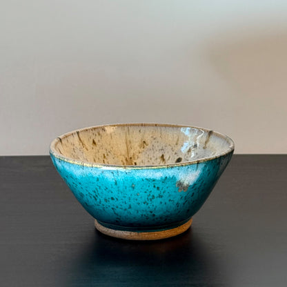 Handmade ceramic bowl with a saturated teal exterior and a creamy speckled interior, finished with a wide rounded profile and glossy glaze.