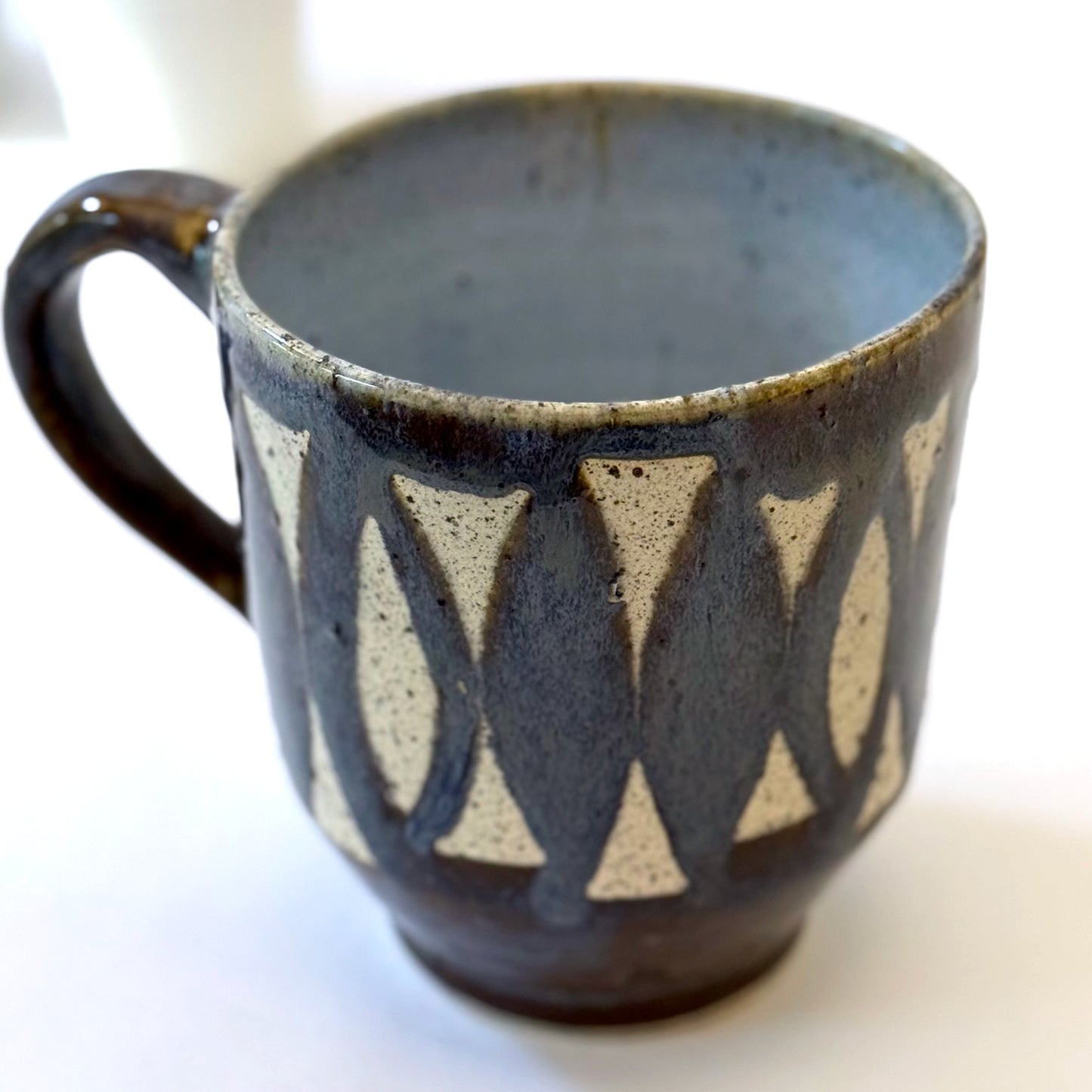 Handmade stoneware mug with repeating surfboard pattern, dark blue glaze, and exposed speckled clay.