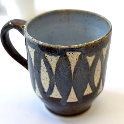 Handmade stoneware mug with repeating surfboard pattern, dark blue glaze, and exposed speckled clay.
