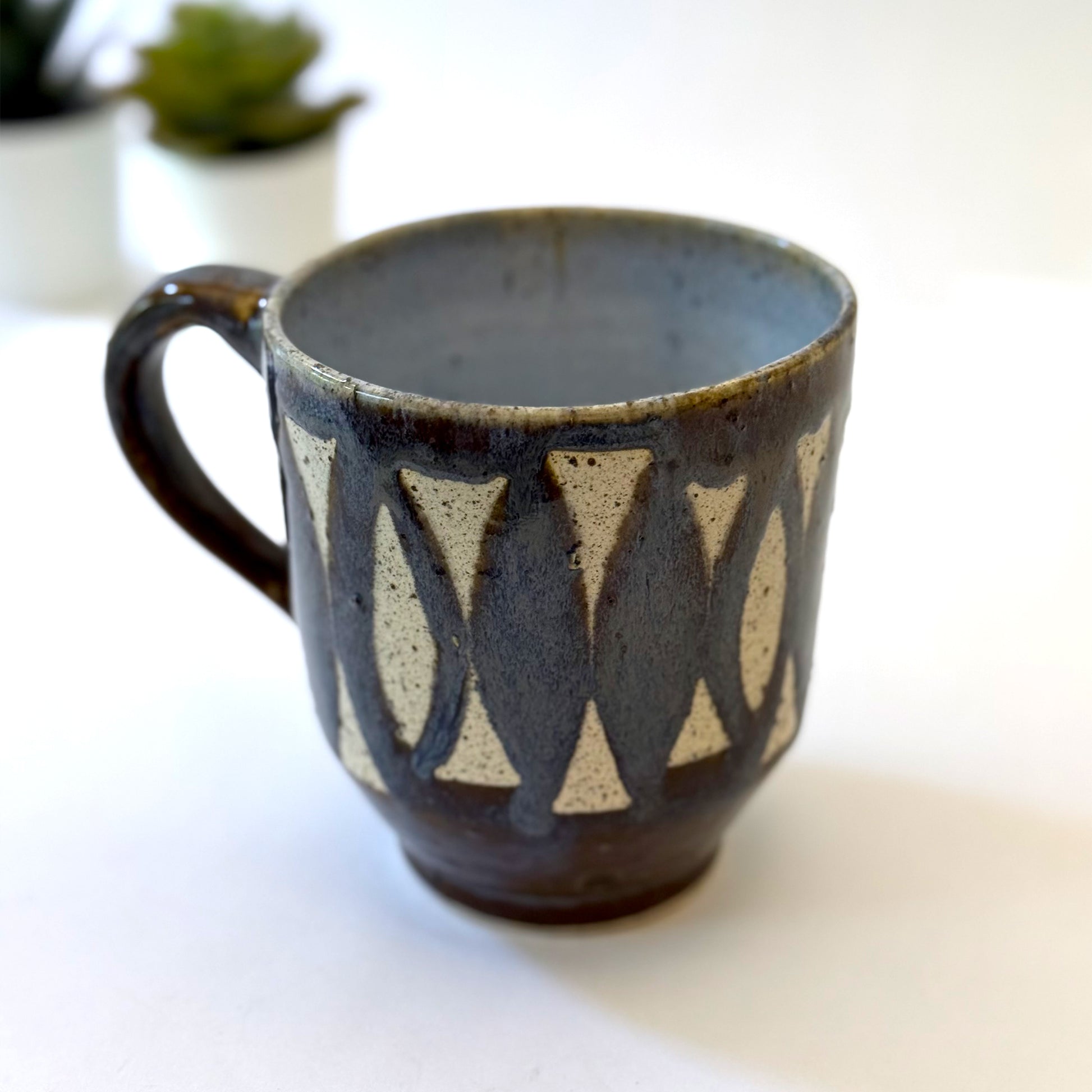 Handmade stoneware mug with repeating surfboard pattern, dark blue glaze, and exposed speckled clay.