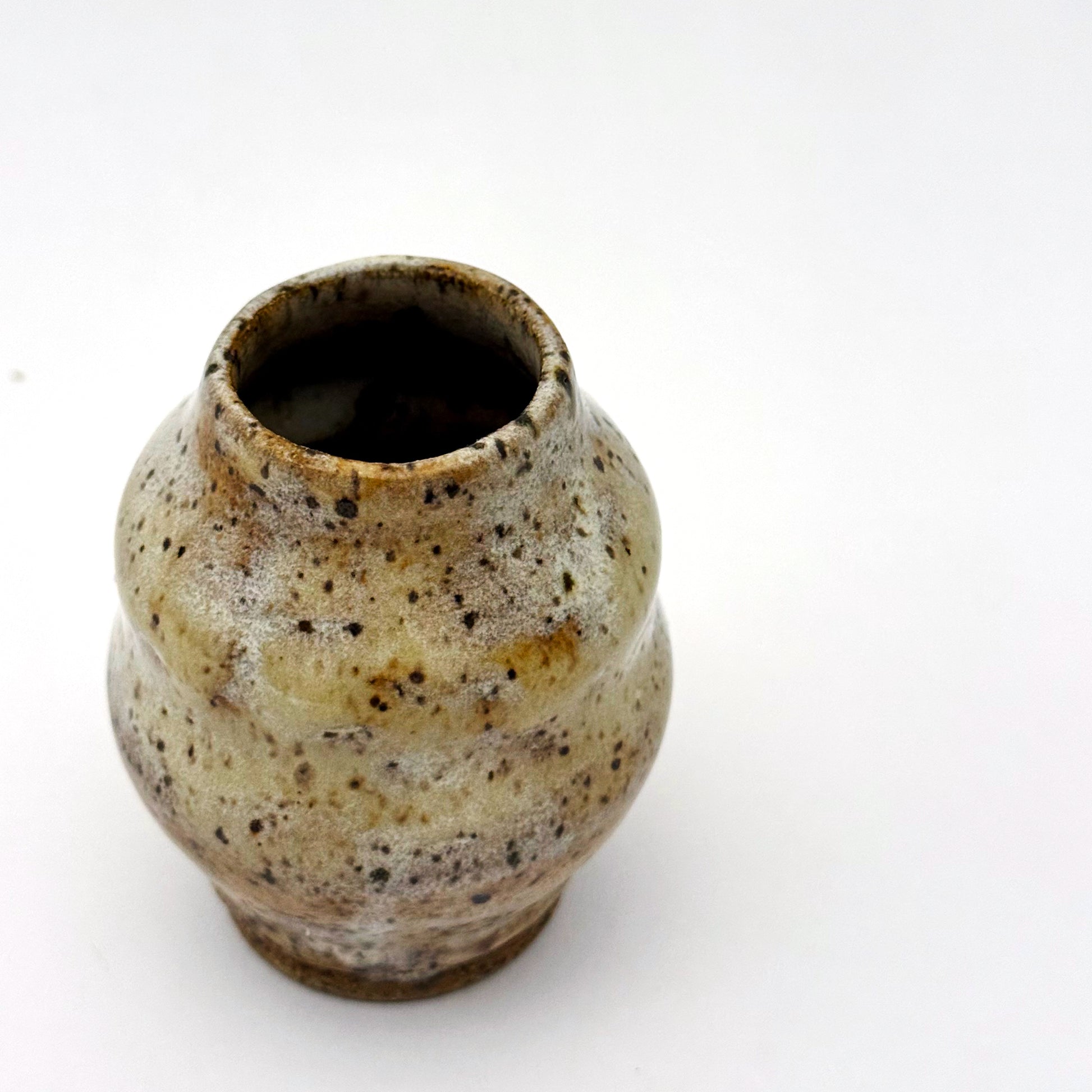 Small handmade stoneware bud vase with rounded shape and narrow opening, finished in a warm speckled glaze in cream, tan, and brown.