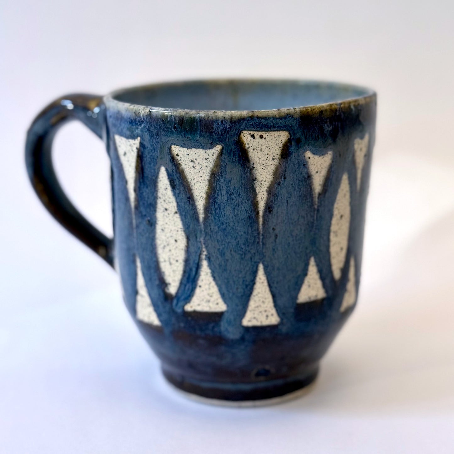 Handmade stoneware mug with repeating surfboard pattern, dark blue glaze, and exposed speckled clay.