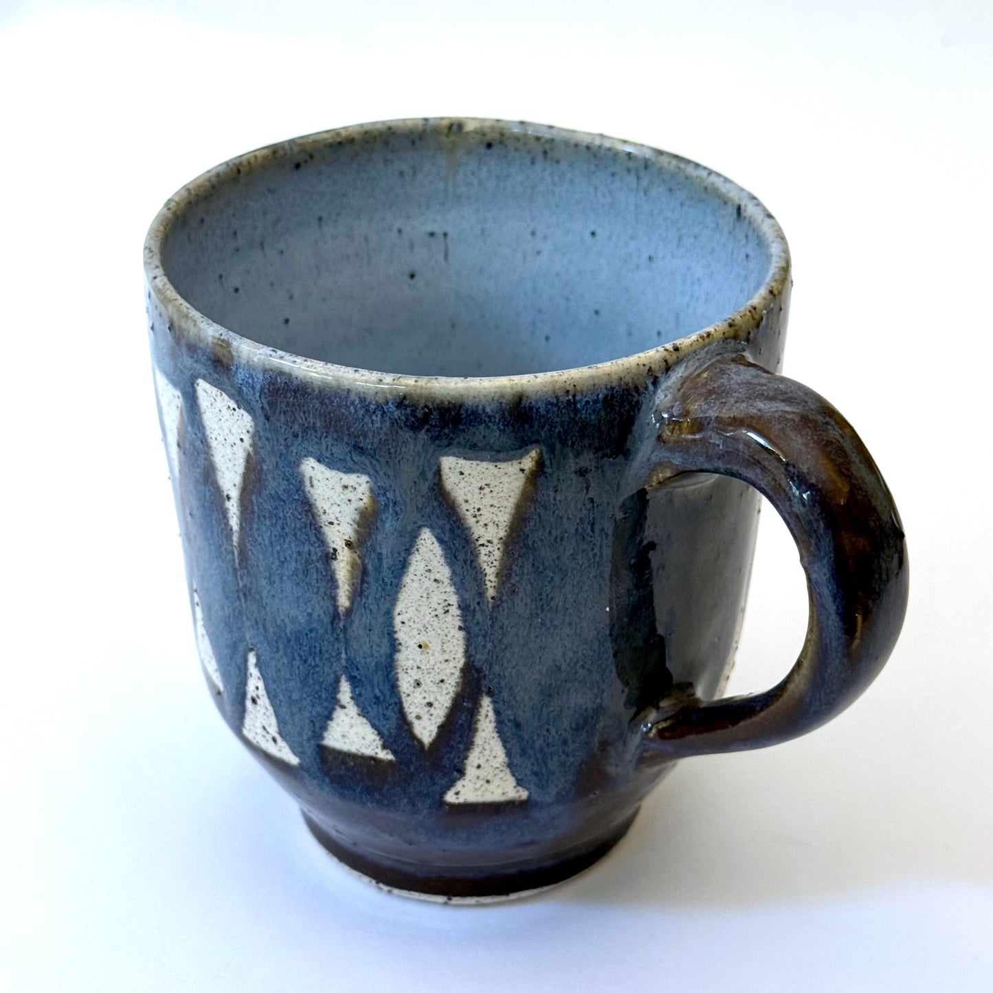 Handmade stoneware mug with repeating surfboard pattern, dark blue glaze, and exposed speckled clay.