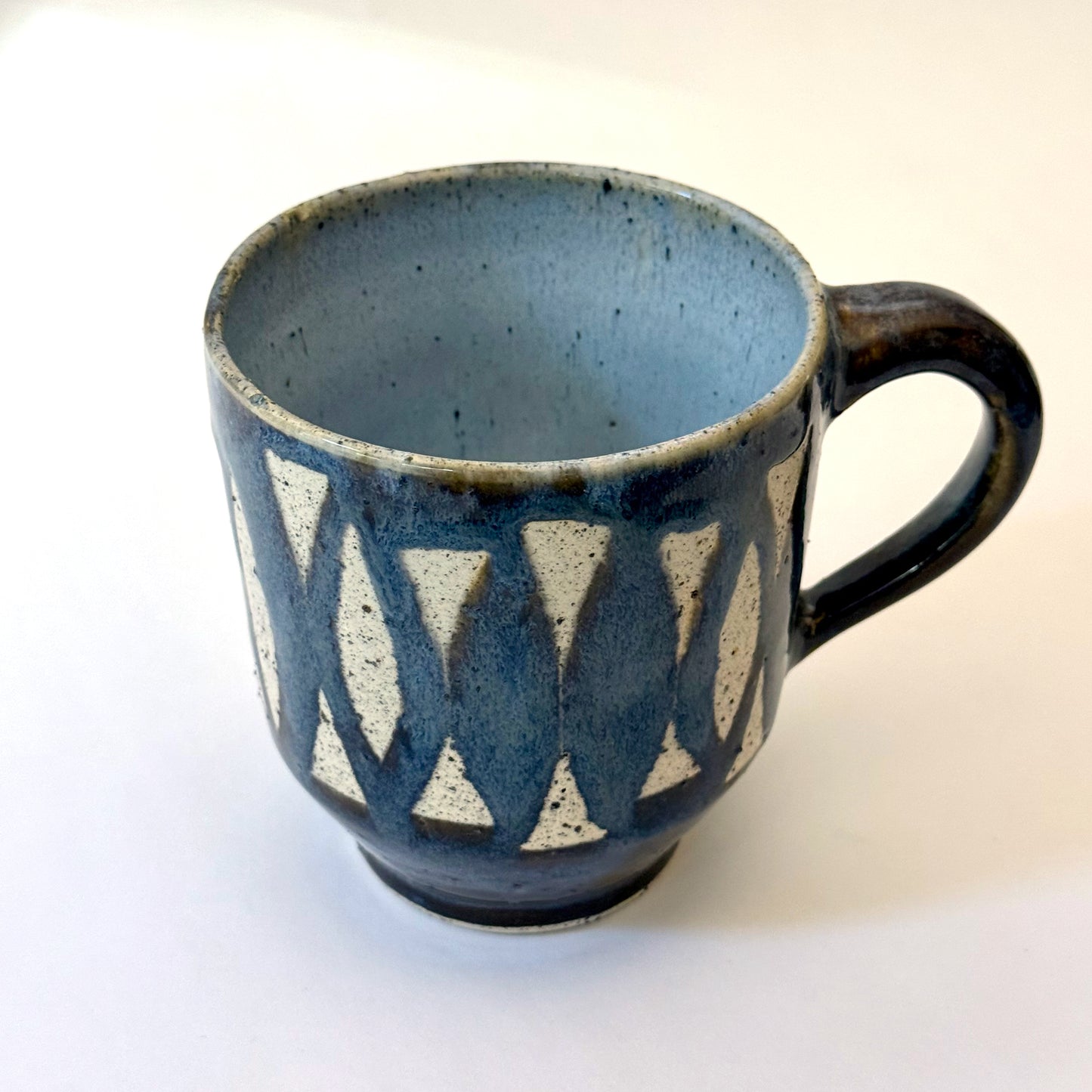 Handmade stoneware mug with repeating surfboard pattern, dark blue glaze, and exposed speckled clay.