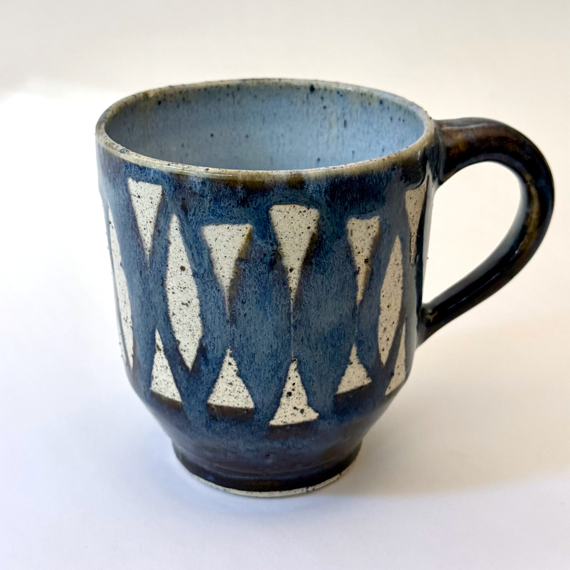 Handmade stoneware mug with repeating surfboard pattern, dark blue glaze, and exposed speckled clay.