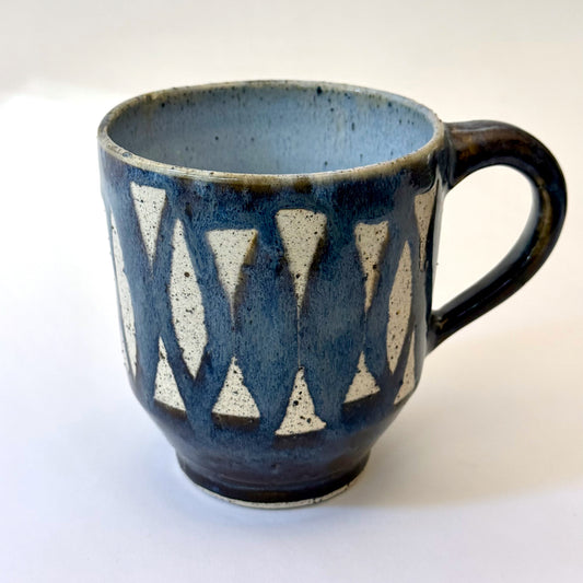 Handmade stoneware mug with repeating surfboard pattern, dark blue glaze, and exposed speckled clay.