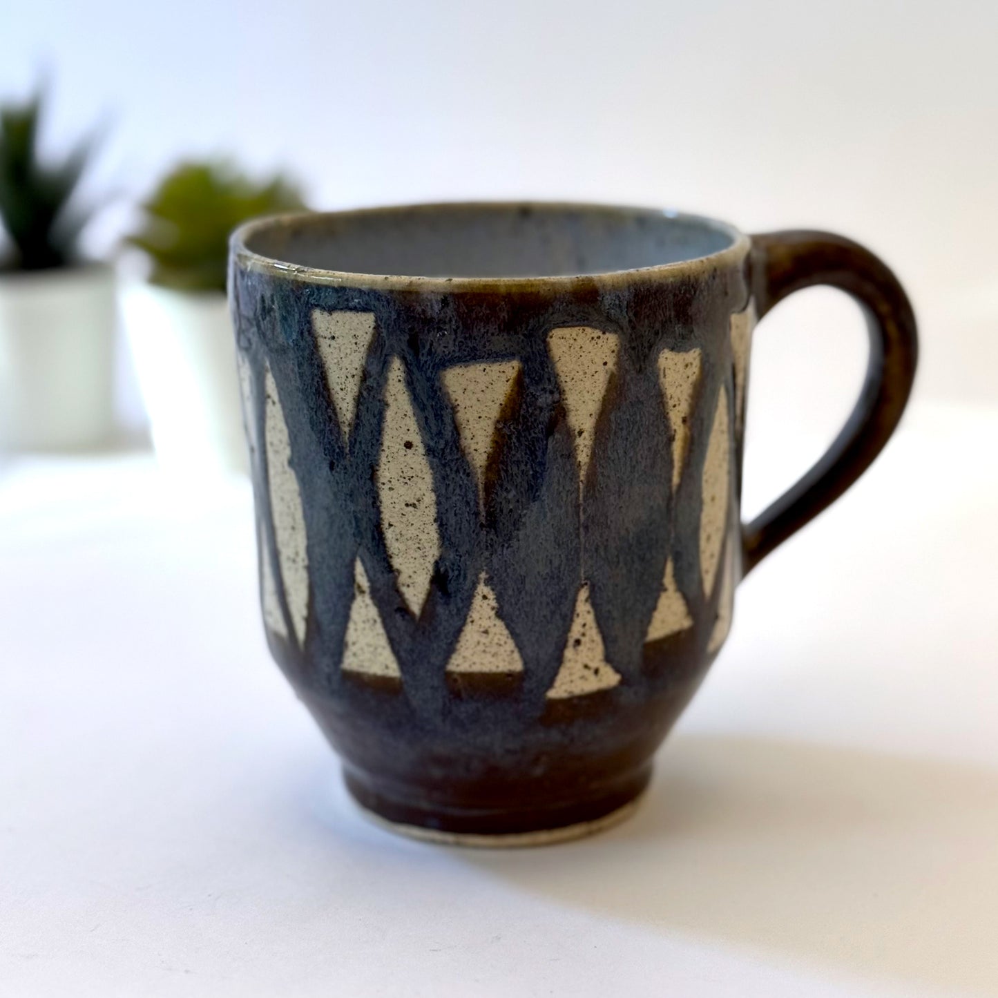 Handmade stoneware mug with repeating surfboard pattern, dark blue glaze, and exposed speckled clay.