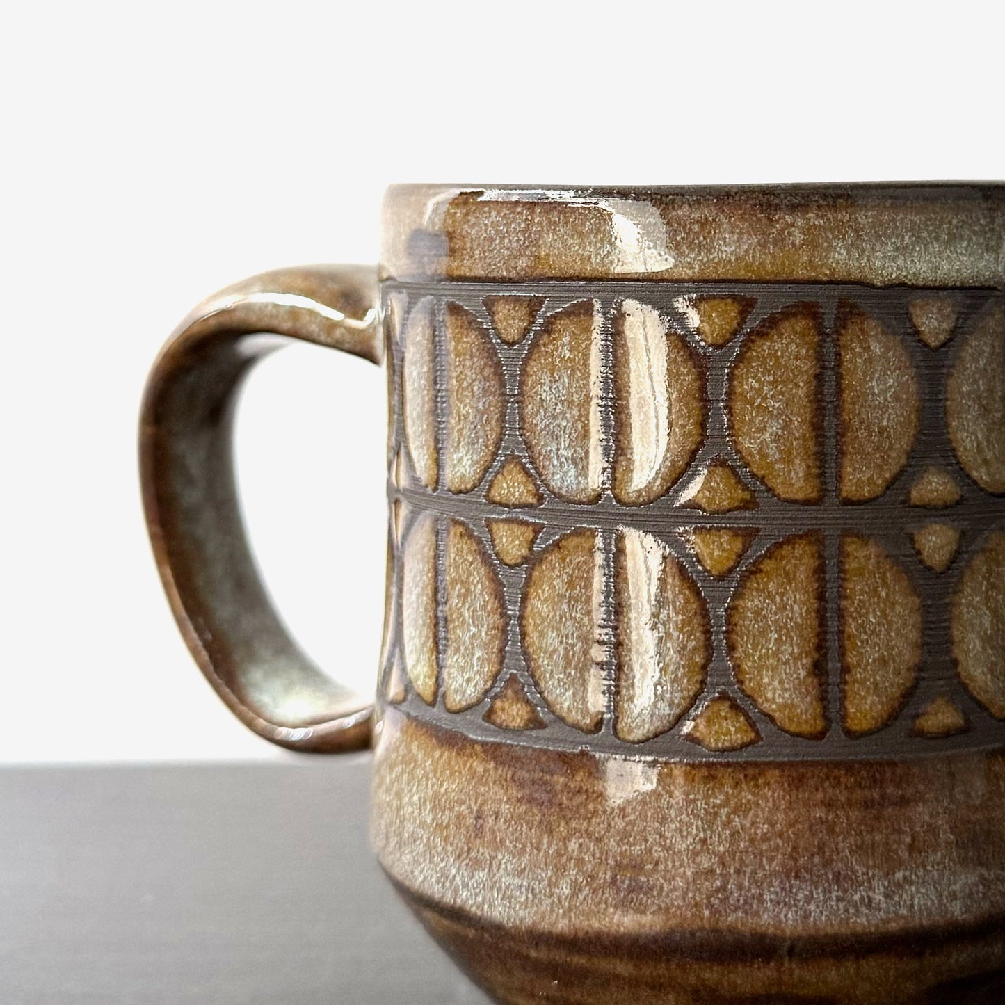 Close up of handmade ceramic mug with a repeating Split Circle breeze block pattern, dark clay showing through the design, and a warm earthy glaze.