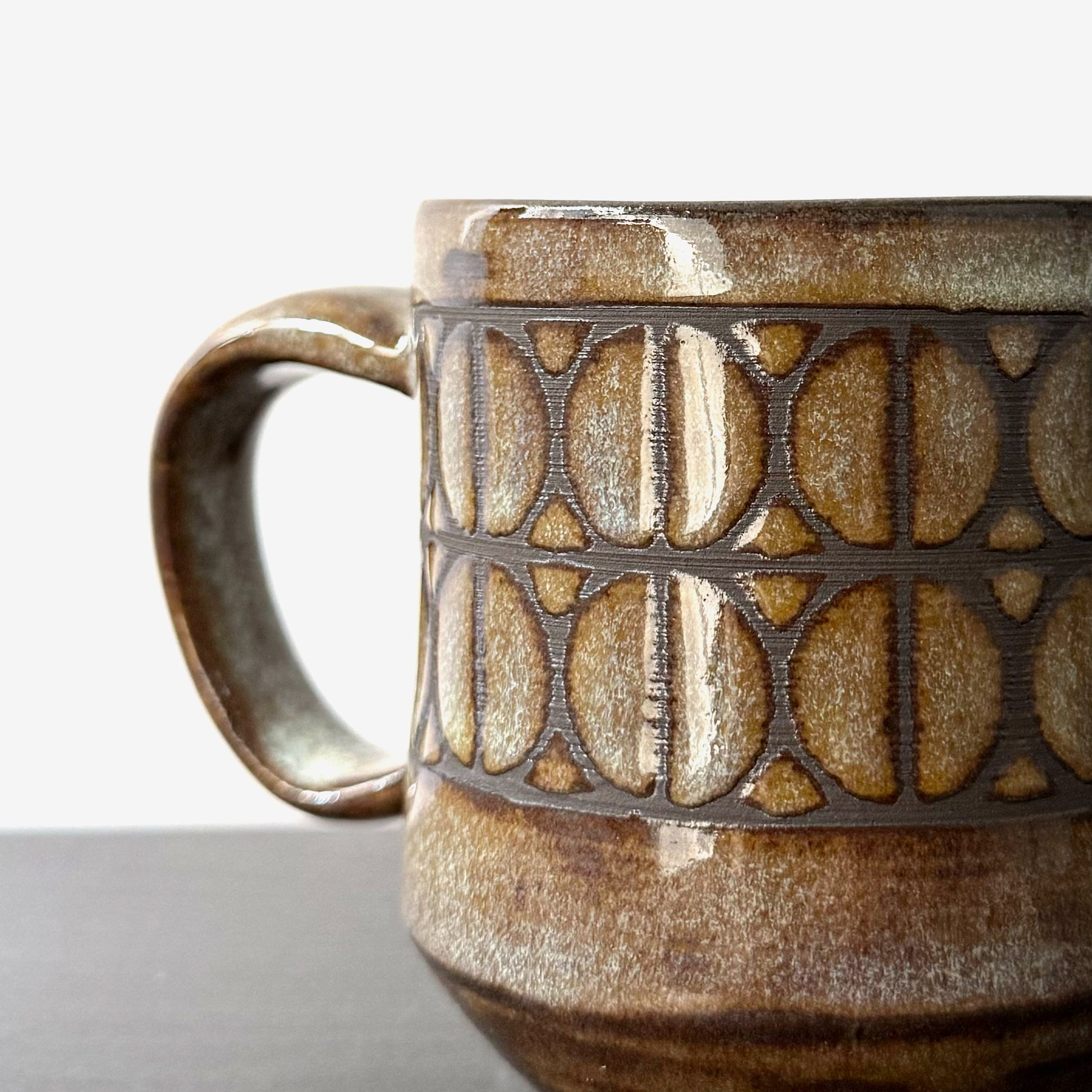 Close up of handmade ceramic mug with a repeating Split Circle breeze block pattern, dark clay showing through the design, and a warm earthy glaze.