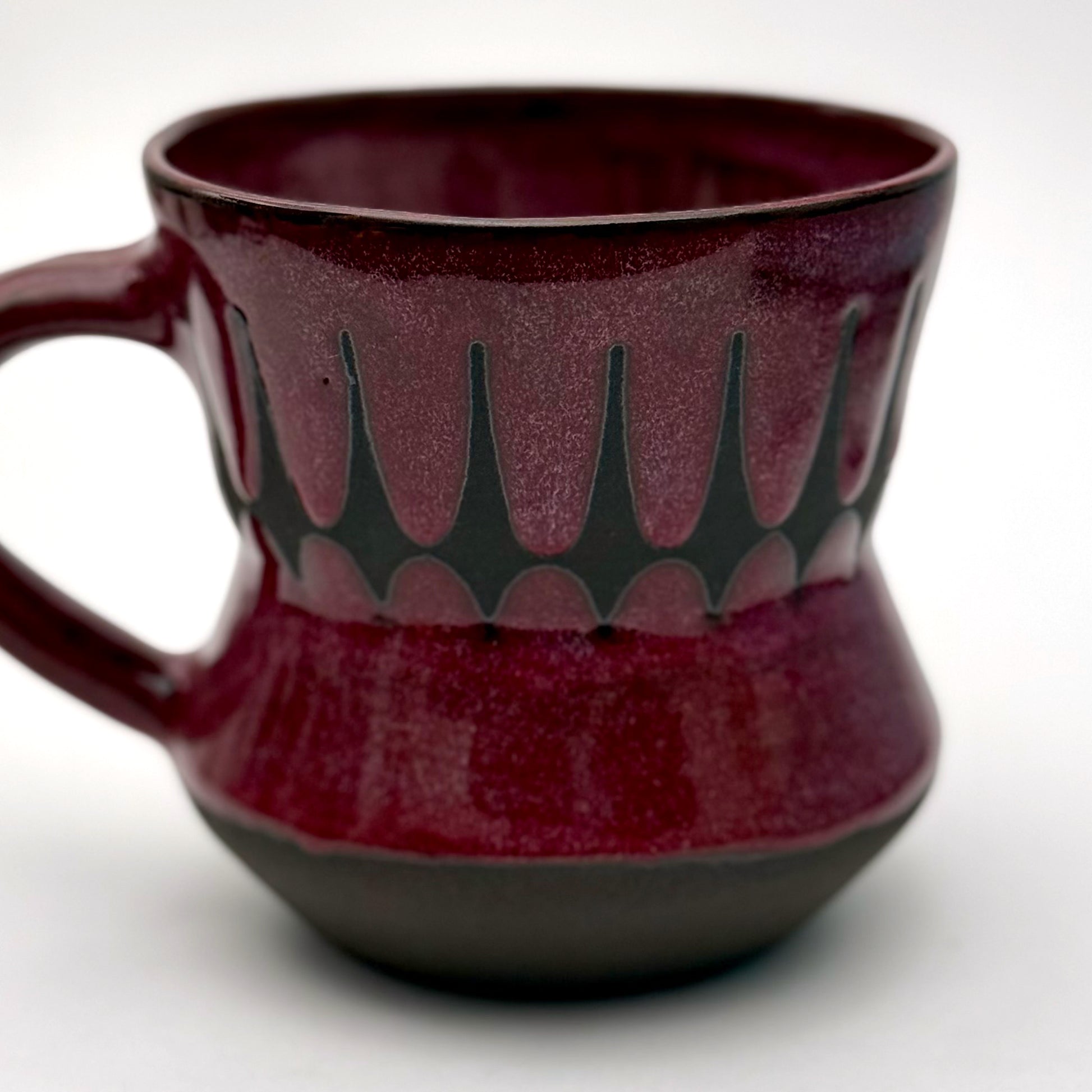 Handmade ceramic mug finished in a rich red glaze with a mid-century–inspired patterned band.