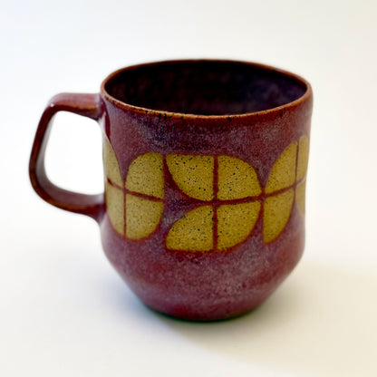 A sturdy, red-glazed mug featuring a repeating geometric tulip pattern in raw, speckled tan stoneware. The design uses sharp lines and a bold, angular handle to create a retro, architectural silhouette.