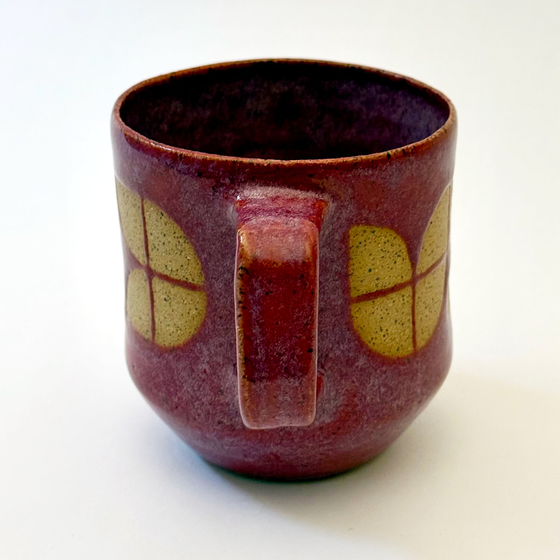 A sturdy, red-glazed mug featuring a repeating geometric tulip pattern in raw, speckled tan stoneware. The design uses sharp lines and a bold, angular handle to create a retro, architectural silhouette.