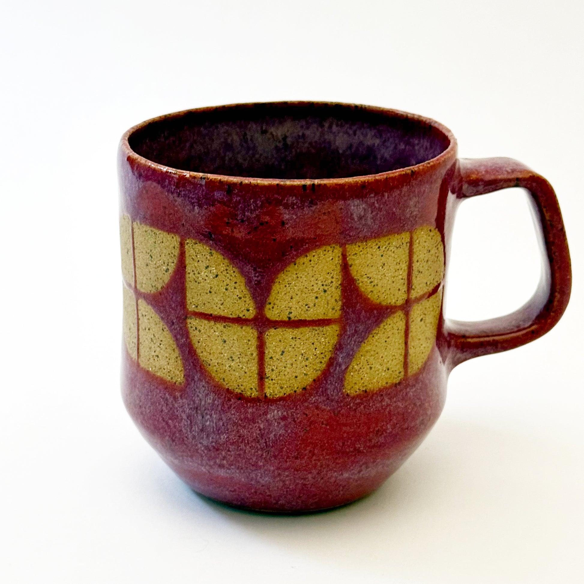 A sturdy, red-glazed mug featuring a repeating geometric tulip pattern in raw, speckled tan stoneware. The design uses sharp lines and a bold, angular handle to create a retro, architectural silhouette.