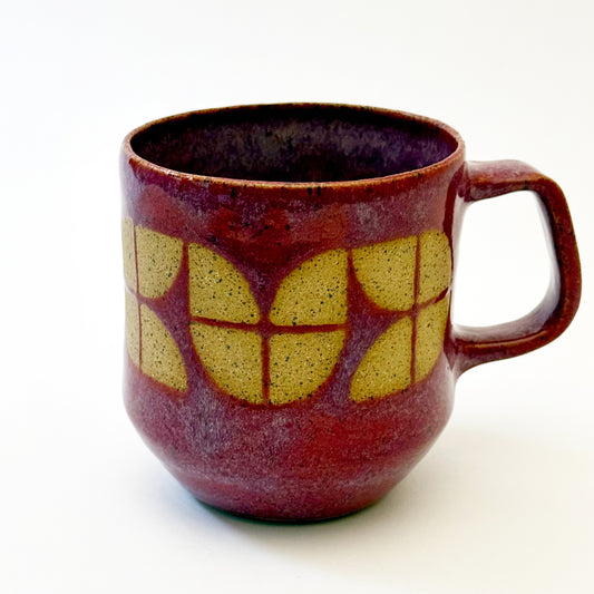 A sturdy, red-glazed mug featuring a repeating geometric tulip pattern in raw, speckled tan stoneware. The design uses sharp lines and a bold, angular handle to create a retro, architectural silhouette.