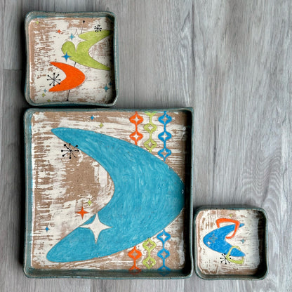 Set of three decorative trays with mid century designs on a wooden background