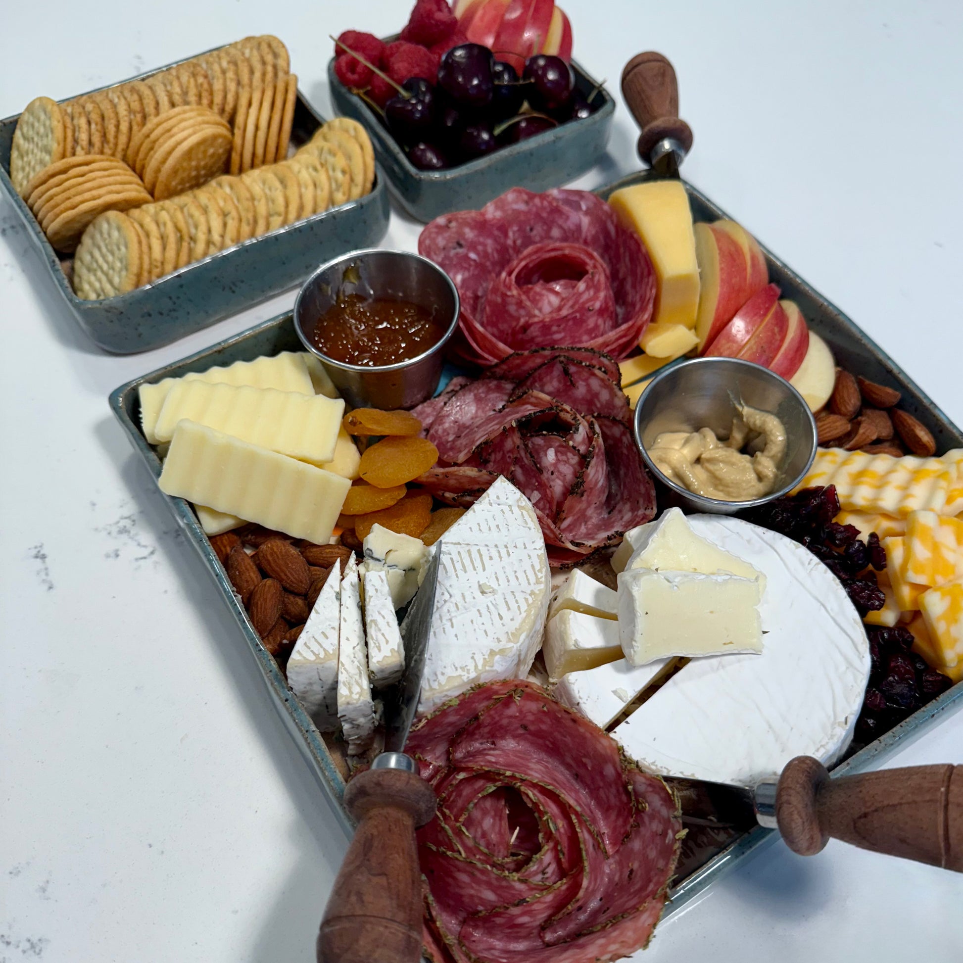 Charcuterie board with meats, cheeses, fruits, and crackers on a white surface.
