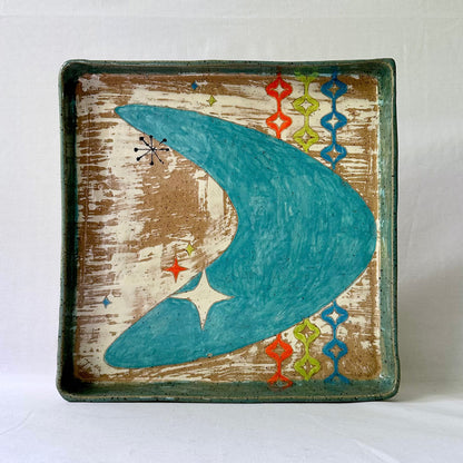 Decorative plate with a blue mid century boomerang and starlite design on a textured brown background