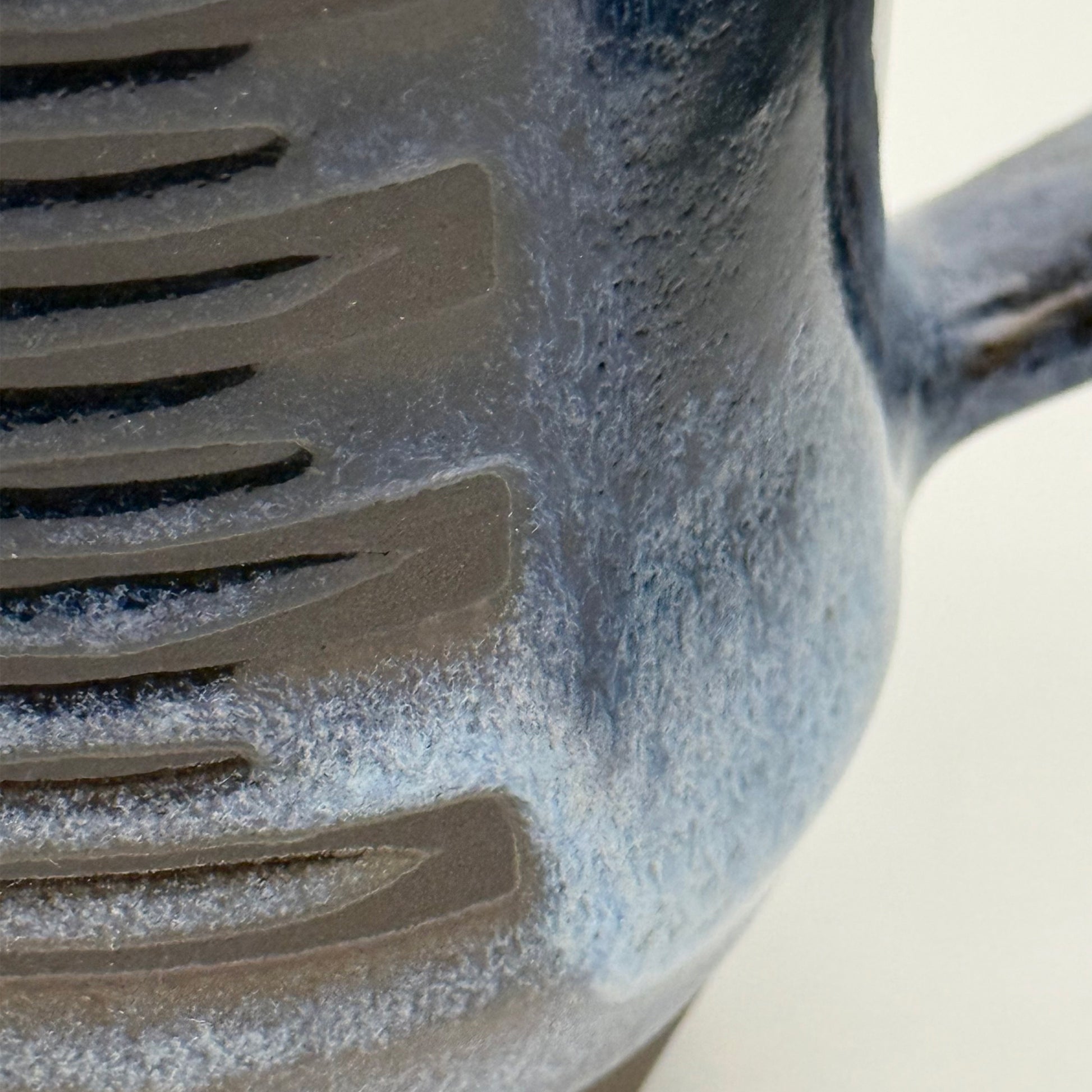 Close-up of handmade ceramic mug with a rounded shape, finished in layered blue glazes and a mid-century–inspired pattern.