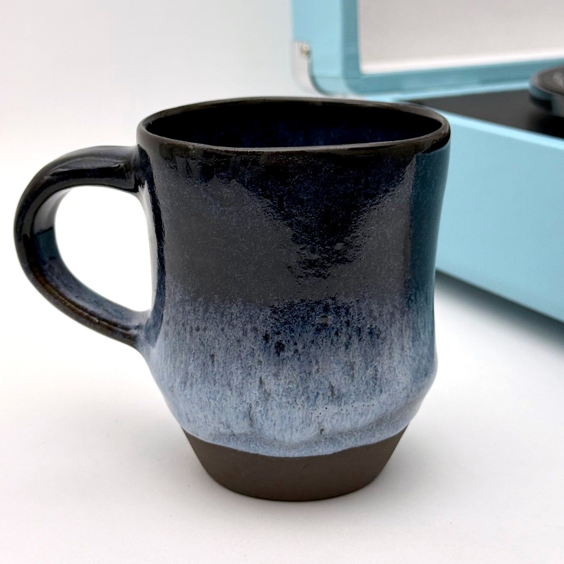 Handmade ceramic mug with a rounded shape, finished in layered blue glazes and a mid-century–inspired pattern.