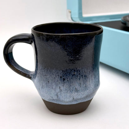 Handmade ceramic mug with a rounded shape, finished in layered blue glazes and a mid-century–inspired pattern.