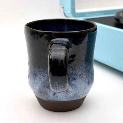 Handmade ceramic mug with a rounded shape, finished in layered blue glazes and a mid-century–inspired pattern.